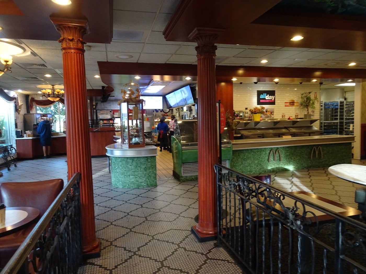 A McDonald's restaurant interior with ornate columns, green-tiled counters, vintage-style decor, and menu screens above the counter. This spot is among the Coolest McDonald's Locations, blending classic architecture with modern fast-food elements.