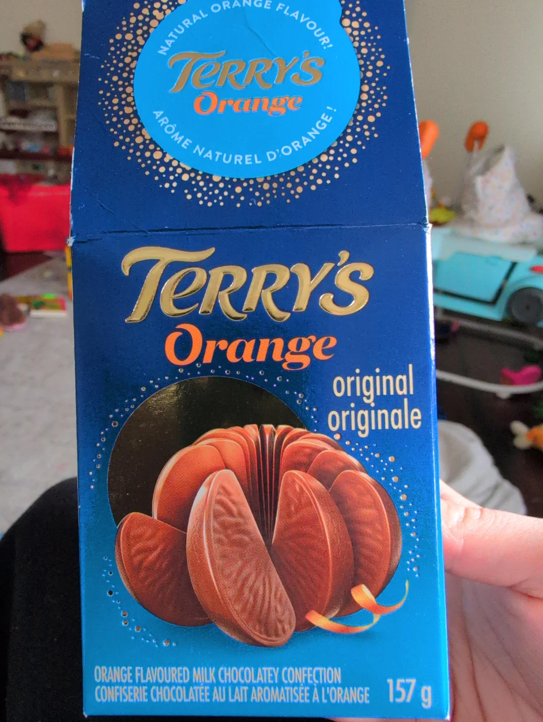 A blue box of Terry's Orange original flavor, showing an image of segmented milk chocolate shaped like an orange. The box displays text in both English and French and contains 157 grams.