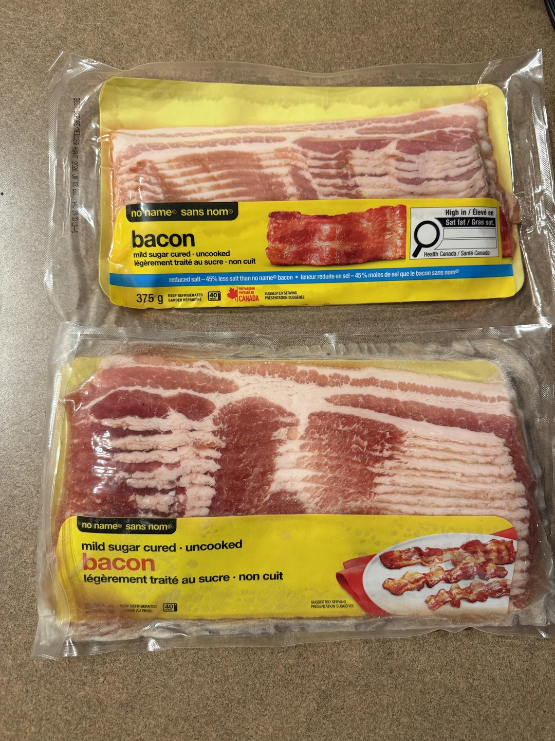 Two packages of uncooked "no name" brand bacon are placed on a countertop. Each package has a yellow label with images of bacon strips and product information in English and French.