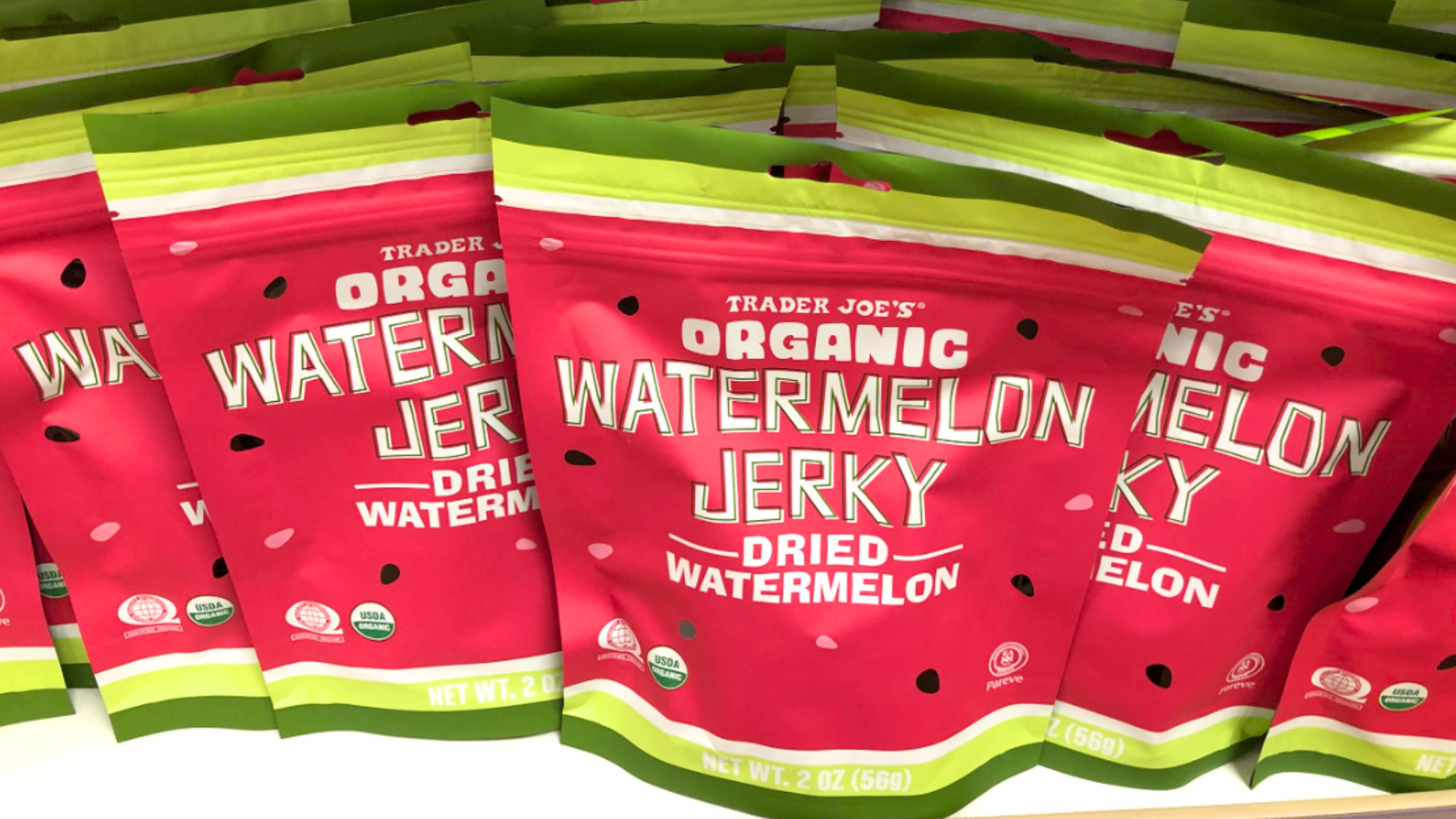 Multiple bags of Trader Joe’s Organic Watermelon Jerky, often listed among Trader Joe's products not worth buying, are displayed in a visually appealing arrangement with red and green packaging decorated with watermelon seed graphics.