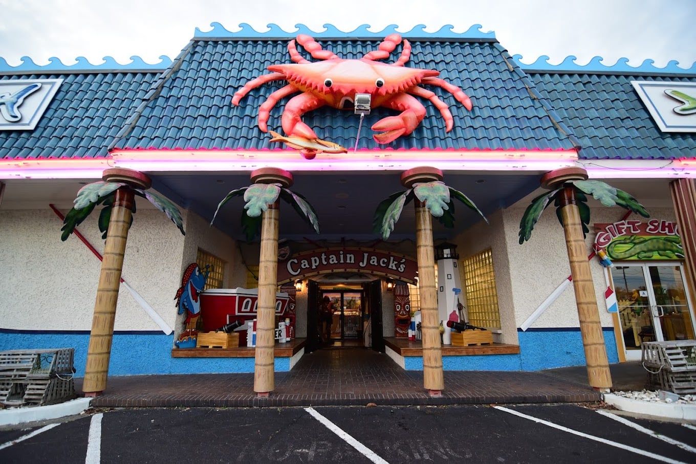 A restaurant entrance with columns resembling palm trees, a large red crab sculpture on the roof, and a sign reading "Captain Jack's." Gift shop signs are visible on the right.