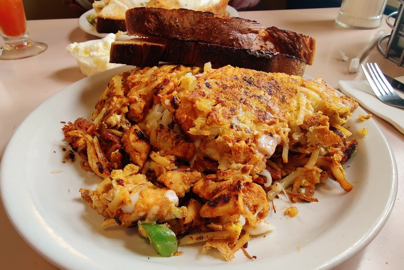 A plate of scrambled eggs with grilled chicken, onions, and green peppers, served with two slices of toasted bread stacked behind the eggs.