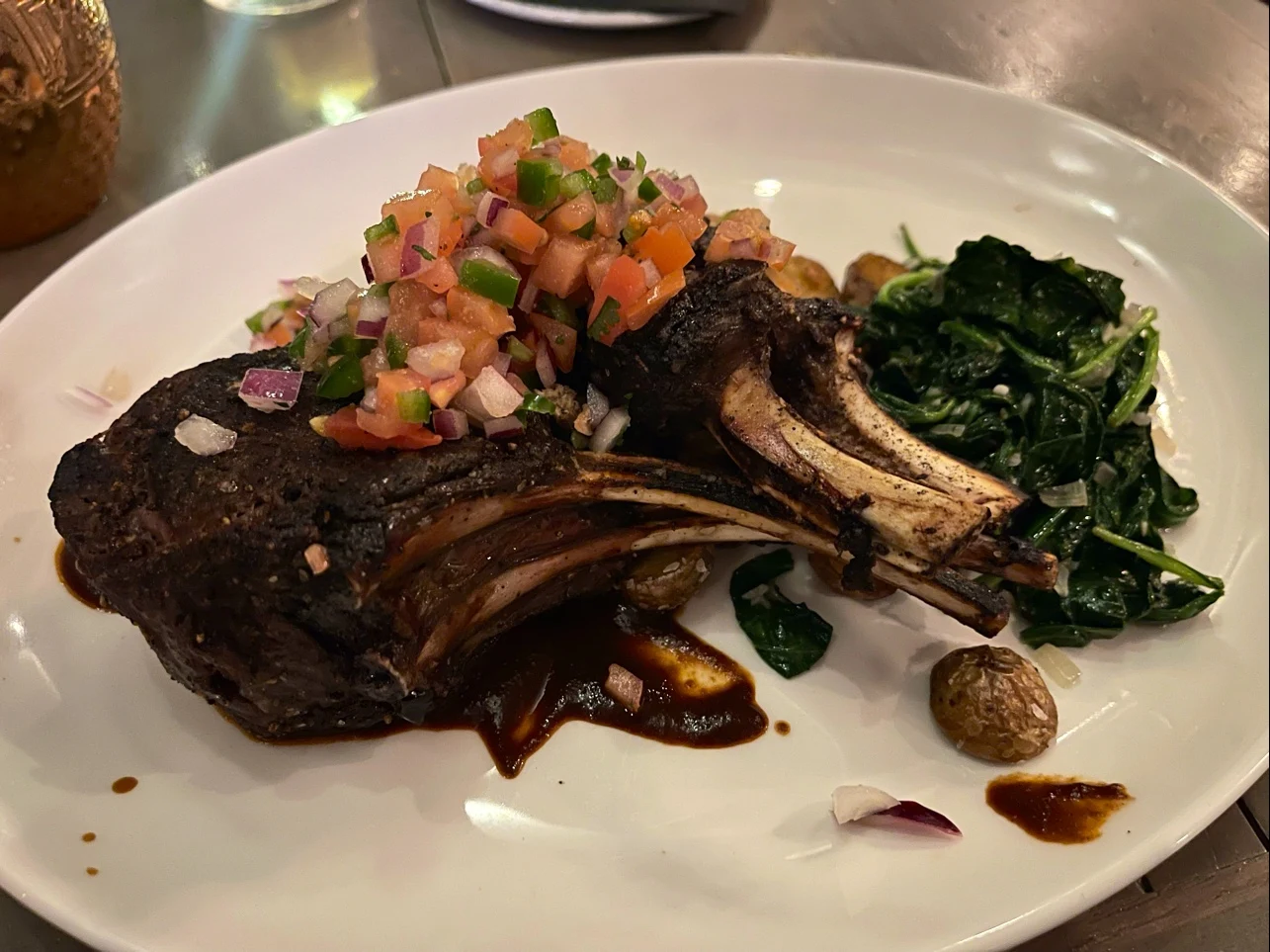 A plate with grilled lamb chops topped with fresh tomato salsa, served with sautéed spinach and roasted baby potatoes on the side.