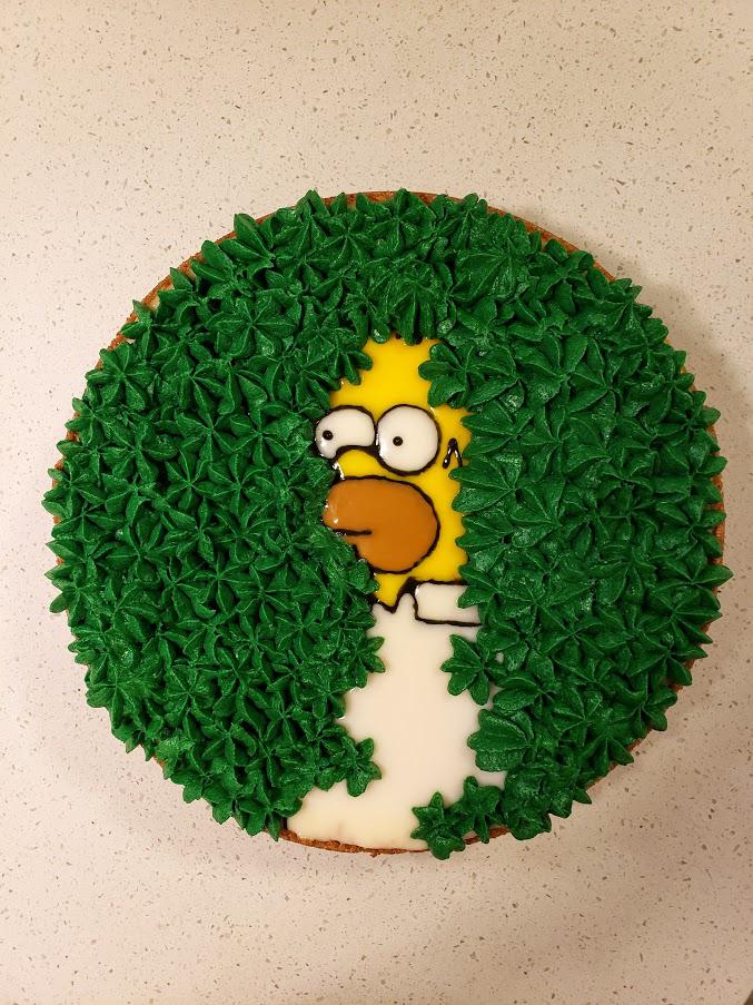 A cake decorated to look like a cartoon man with yellow skin retreating into green bushes, inspired by a famous meme.