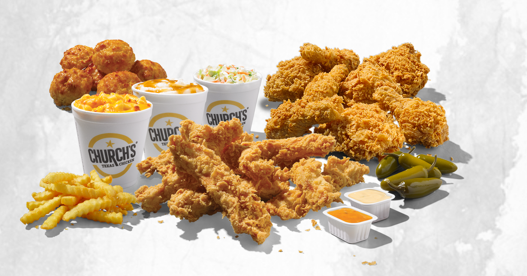 Assorted Church’s Texas Chicken meal from one of the most beloved fried chicken chains, featuring fried chicken, tenders, crinkle-cut fries, biscuits, macaroni and cheese, coleslaw, jalapeños, and dipping sauces—all served in branded containers on a light background.