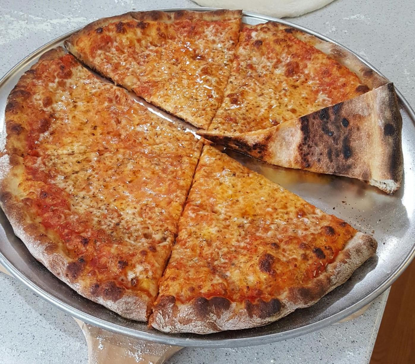 A thin-crust cheese pizza with six slices sits on a metal pizza tray. One slice is slightly separated, showing a crispy, browned crust and melted cheese with herbs.