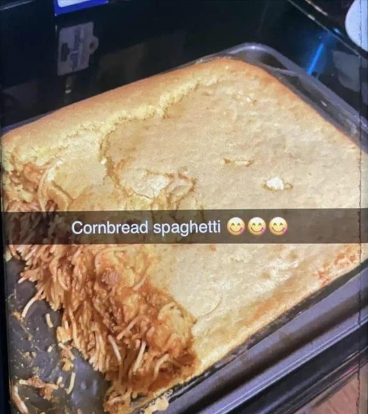 A baking pan filled with cornbread covering spaghetti underneath. A large corner piece is missing, revealing the spaghetti. Text overlay says, "Cornbread spaghetti" with three smiley face emojis.