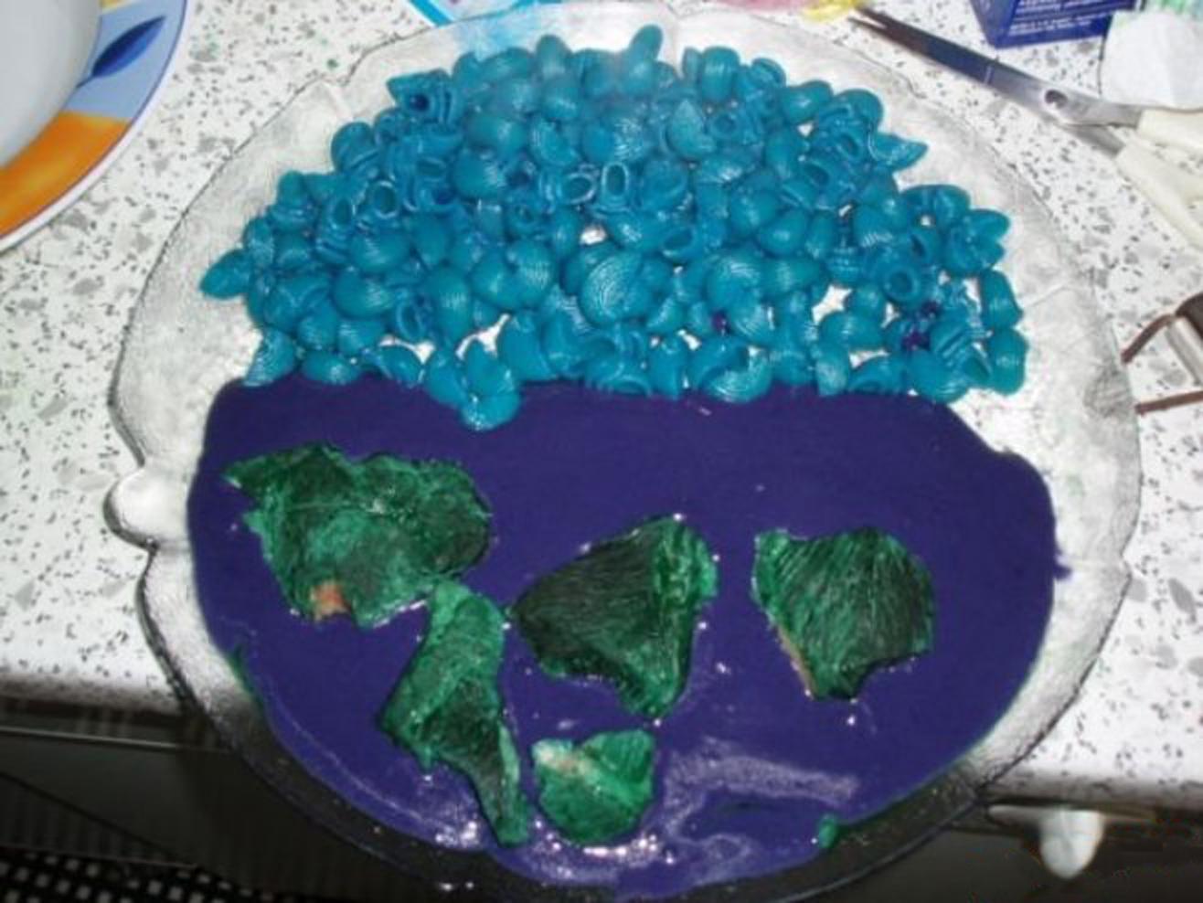 A dish with blue pasta shells and green lumps on purple sauce, arranged to resemble an abstract map or globe, on a speckled countertop.