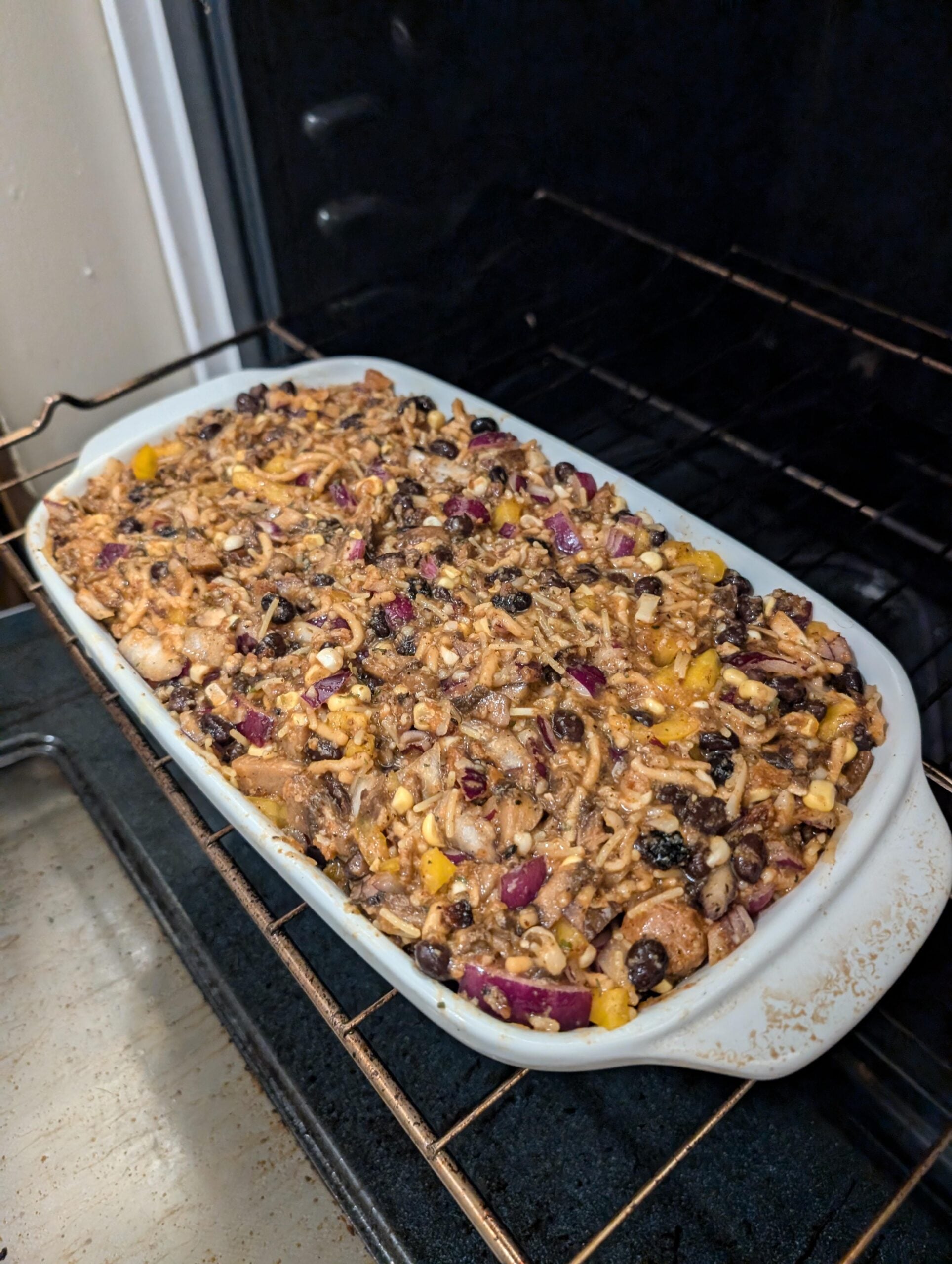 A casserole dish filled with a baked fruit and nut mixture, including visible pieces of pecans, raisins, and chopped fruit, sits on an oven rack.