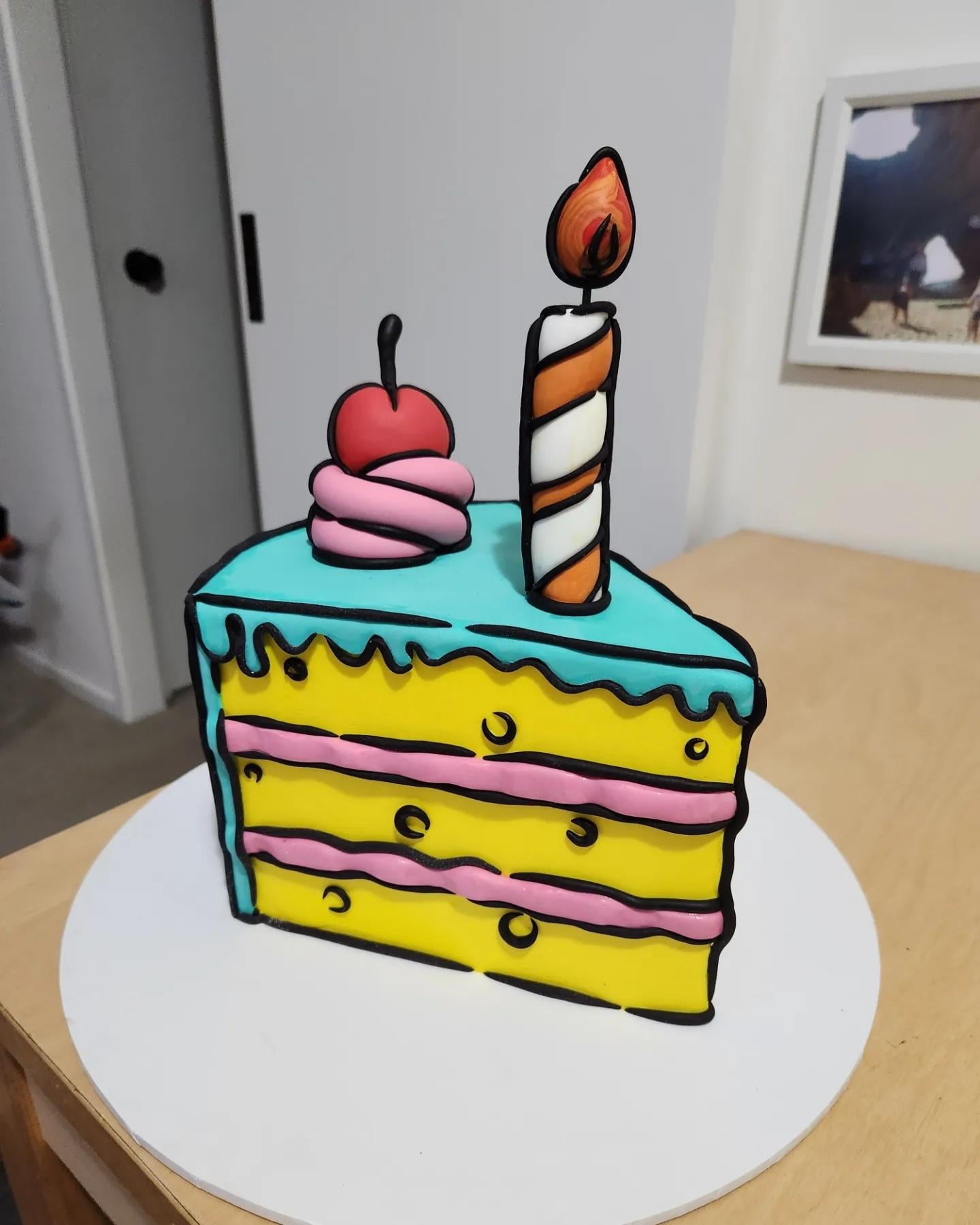 A cartoon-style slice of birthday cake with blue icing, pink filling, a cherry on top, and a striped candle, sitting on a white base on a wooden table.