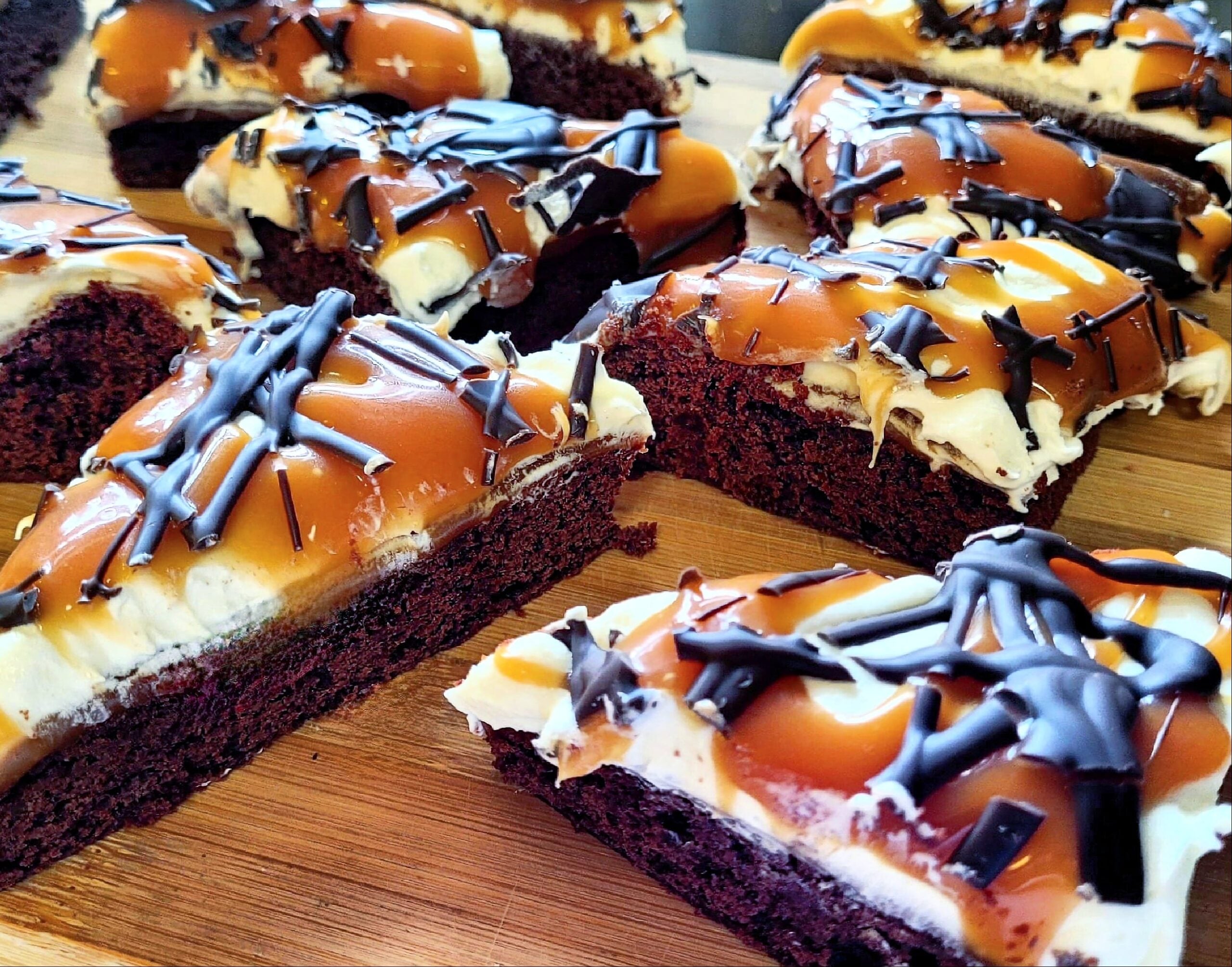 Homemade desserts shine with these chocolate brownies topped with caramel, whipped cream, and chocolate drizzle, beautifully arranged on a wooden surface.