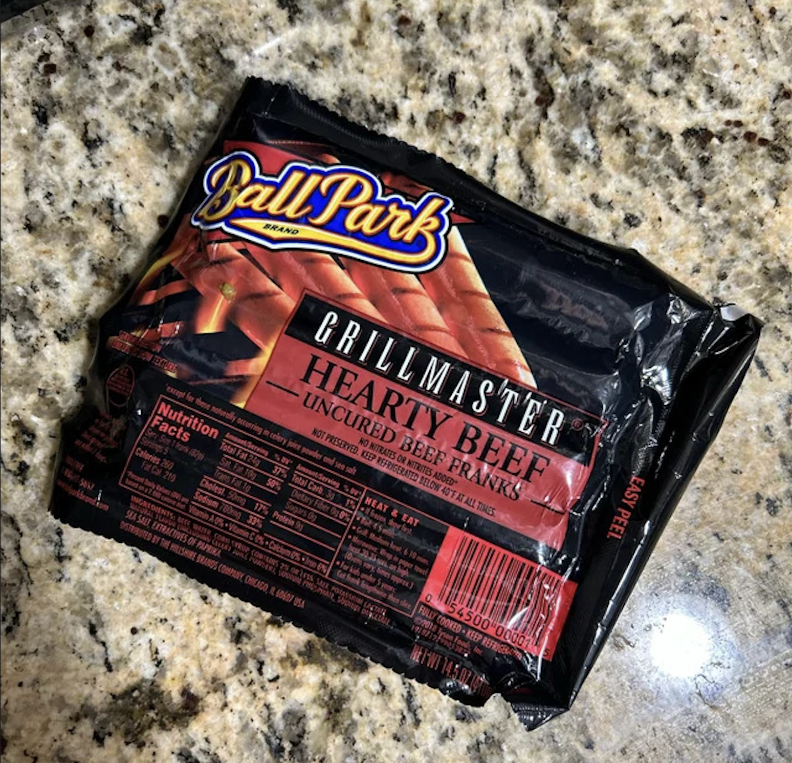 A package of Ball Park Grillmaster Hearty Beef Uncured Beef Franks sits on a speckled granite countertop, with the nutrition facts visible on the left side of the packaging.