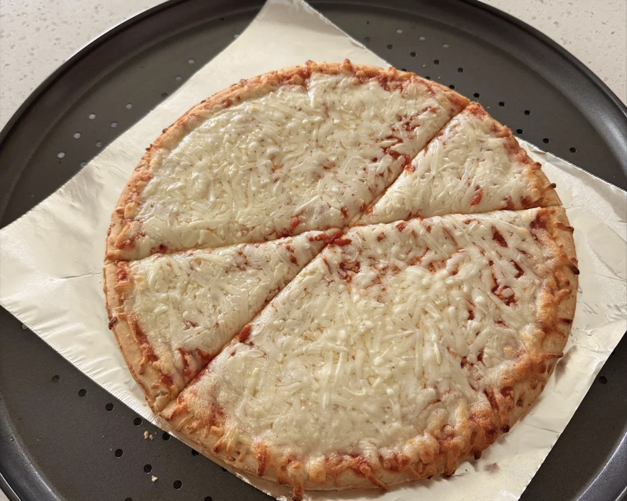 A cheese pizza with four slices on a round baking tray, placed on parchment paper. Perfectly capturing one of the best pizza photos, the image showcases an evenly baked pizza with melted cheese and a thin crust.