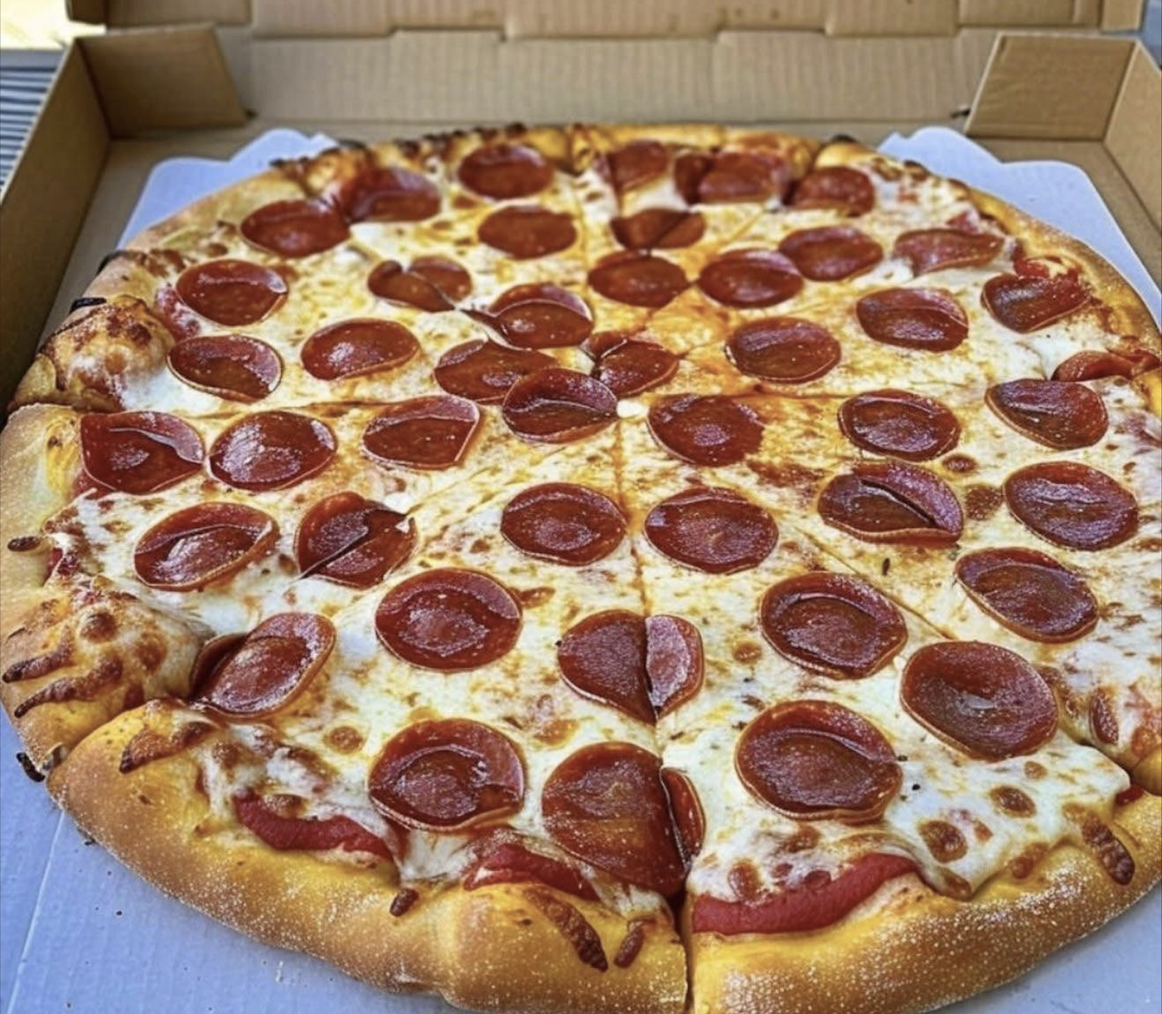 A large pepperoni pizza with melted cheese and evenly spaced pepperoni slices sits in an open cardboard box, ready to be served—capturing one of the best pizza photos you’ll find.