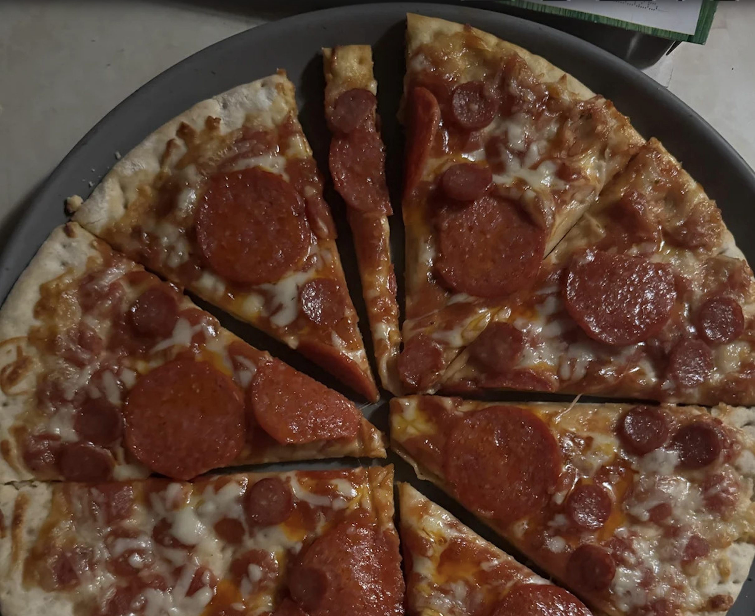 A cooked pepperoni pizza cut into eight slices sits on a round pan. The pizza has melted cheese and both large and small pepperoni slices, making it a mouthwatering contender for the best pizza photos.