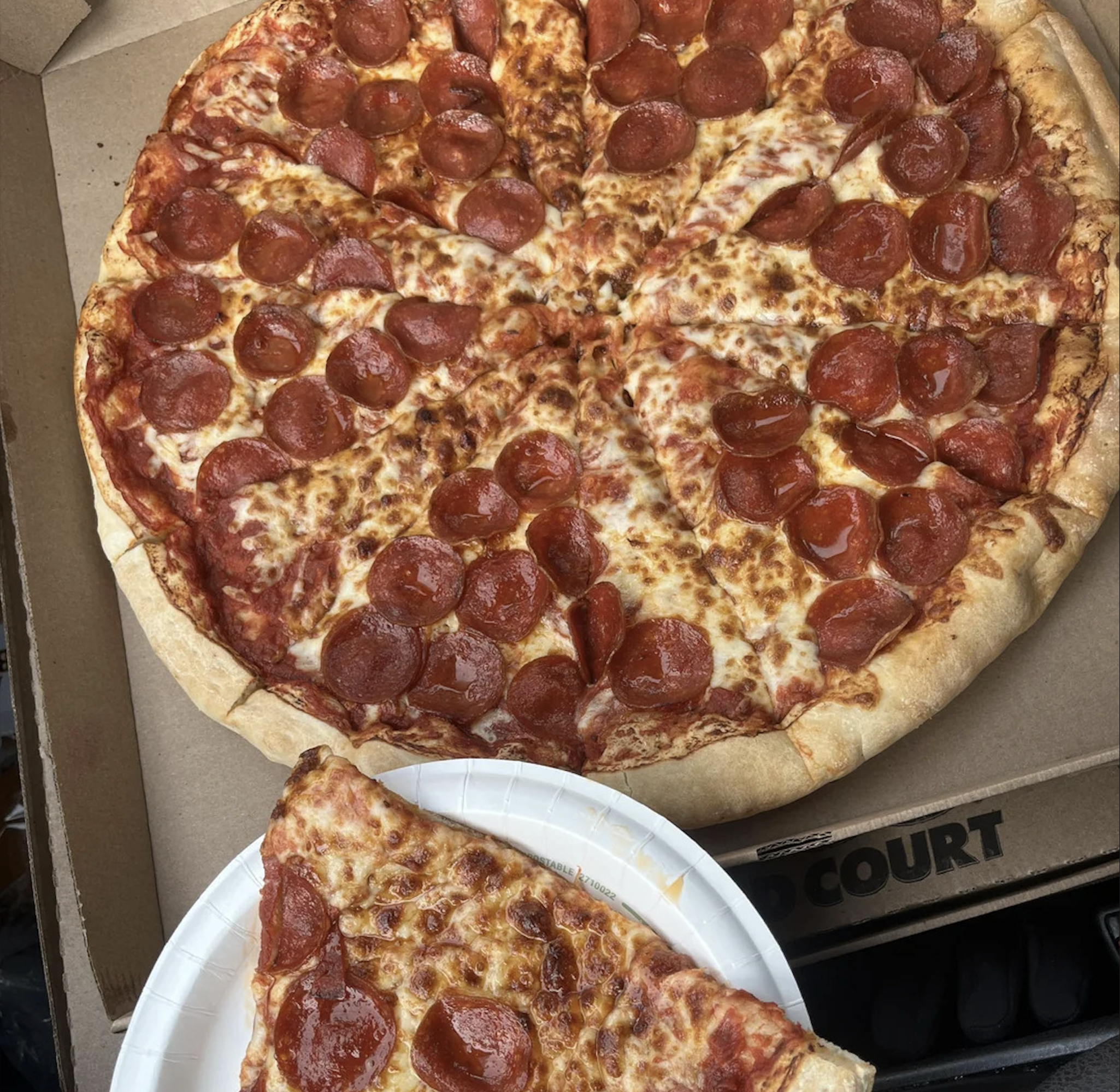 A large pepperoni pizza with one slice taken out and placed on a white paper plate, all inside an open pizza box—an image that truly belongs among the best pizza photos.