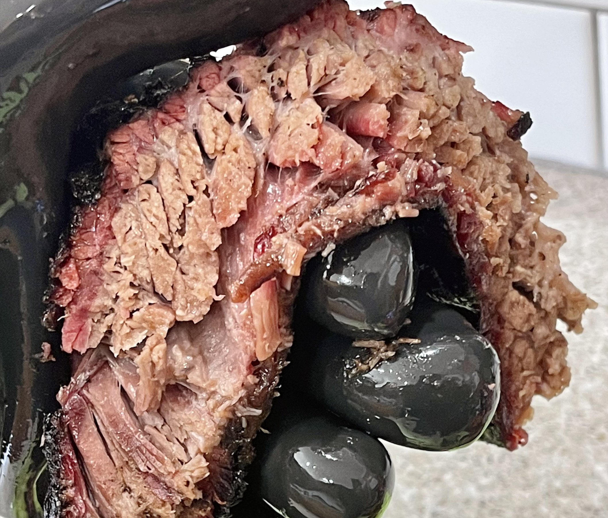 A gloved hand holds a thick, juicy slice of smoked brisket, showing marbled meat with a pink smoke ring and a dark, seasoned bark.