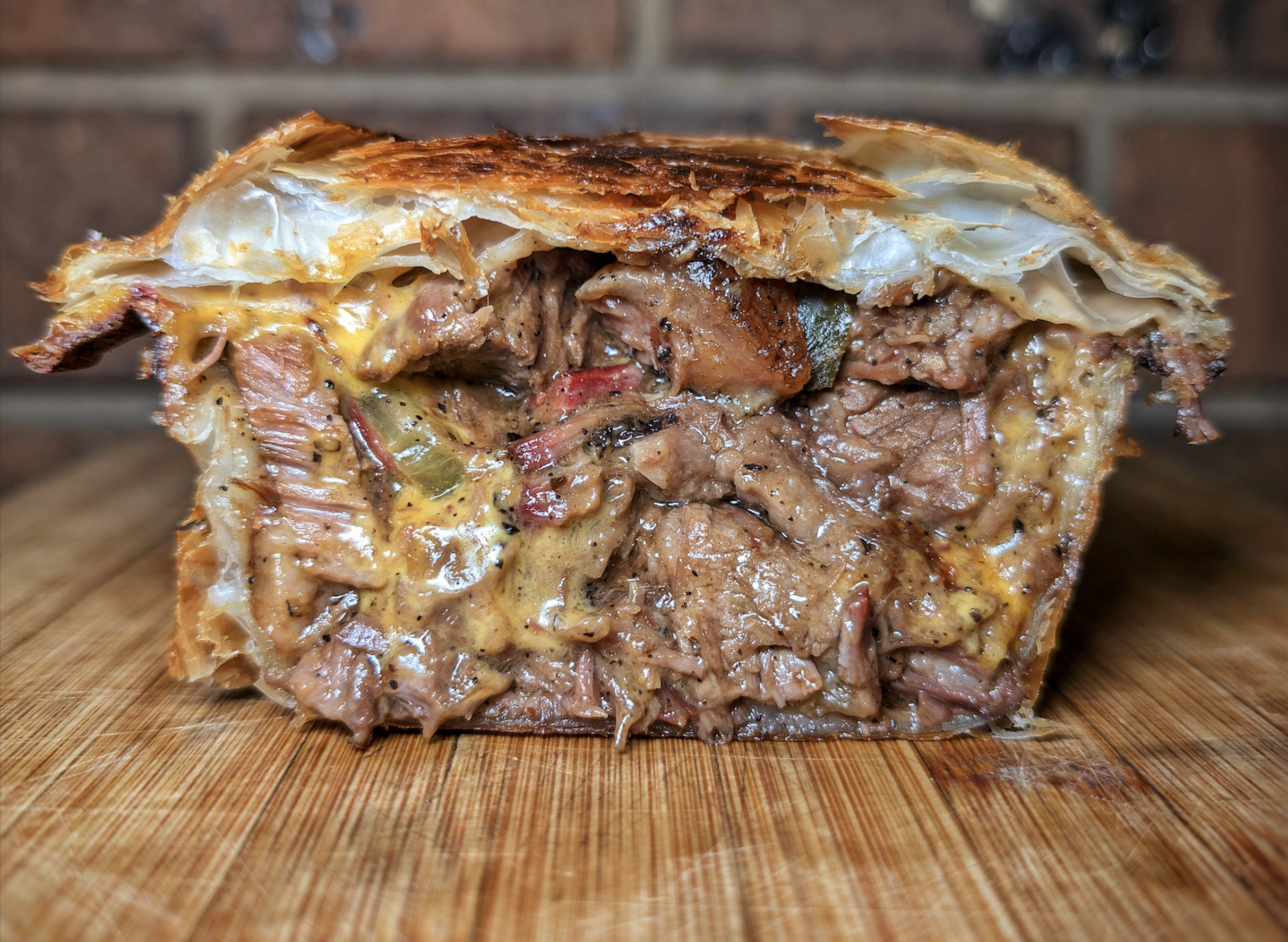 A close-up of a savory meat pie sliced open, showing tender, juicy beef pieces in a thick, rich gravy, wrapped in a golden, flaky pastry crust, on a wooden surface.