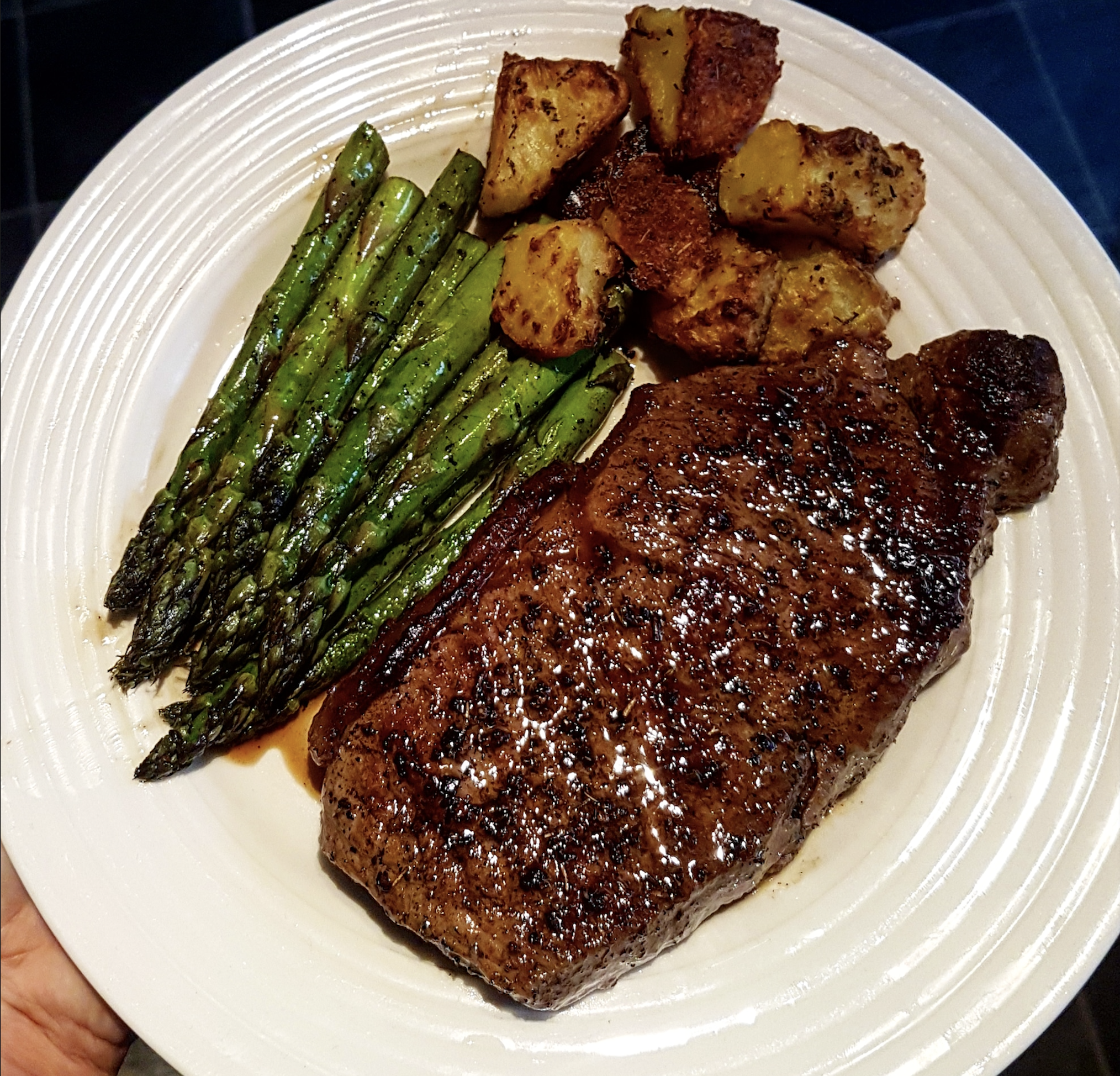 A white plate with a grilled steak, roasted potatoes, and seasoned asparagus spears arranged neatly on it.