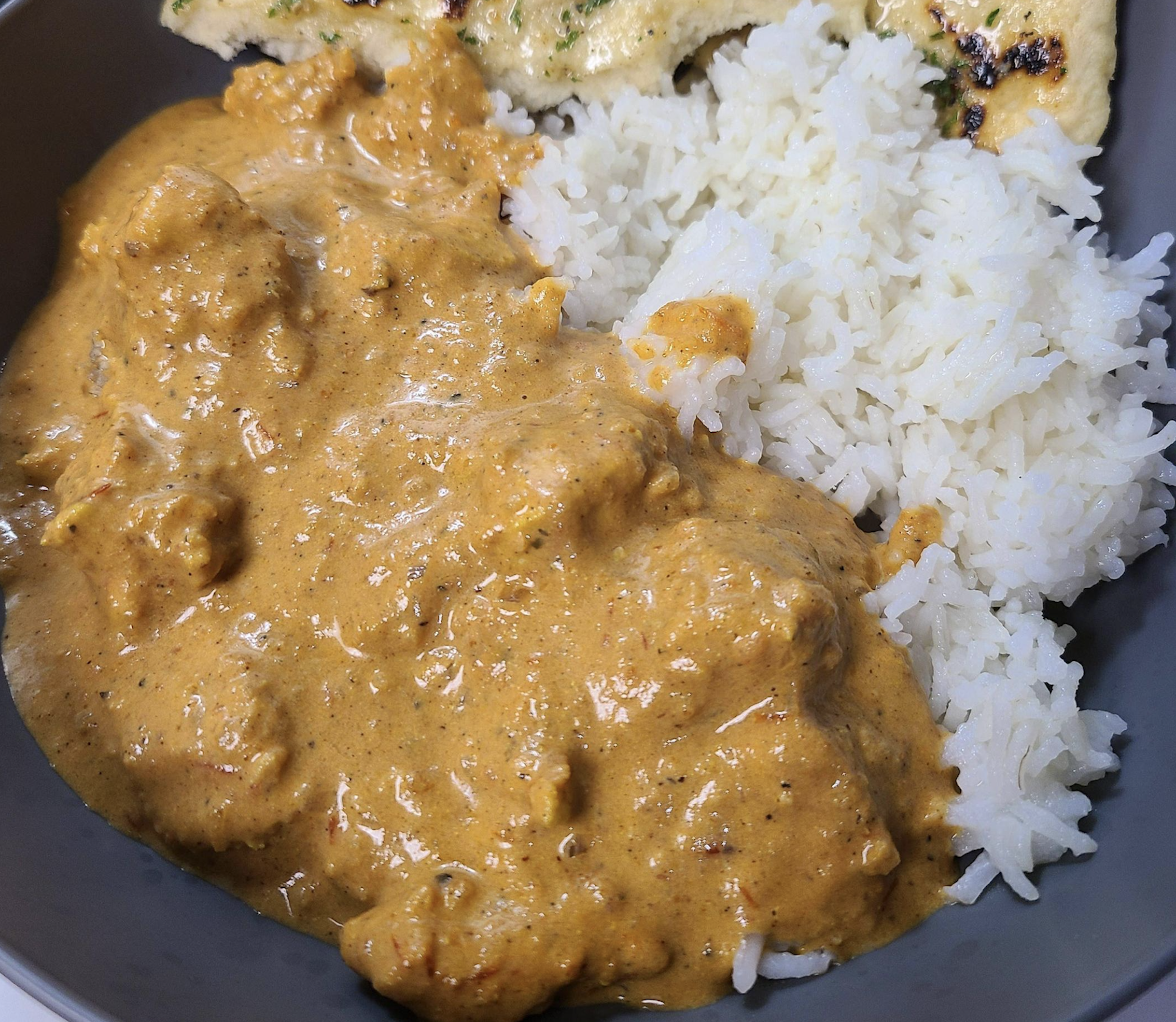 A plate with creamy orange chicken curry, white rice, and a piece of naan bread.