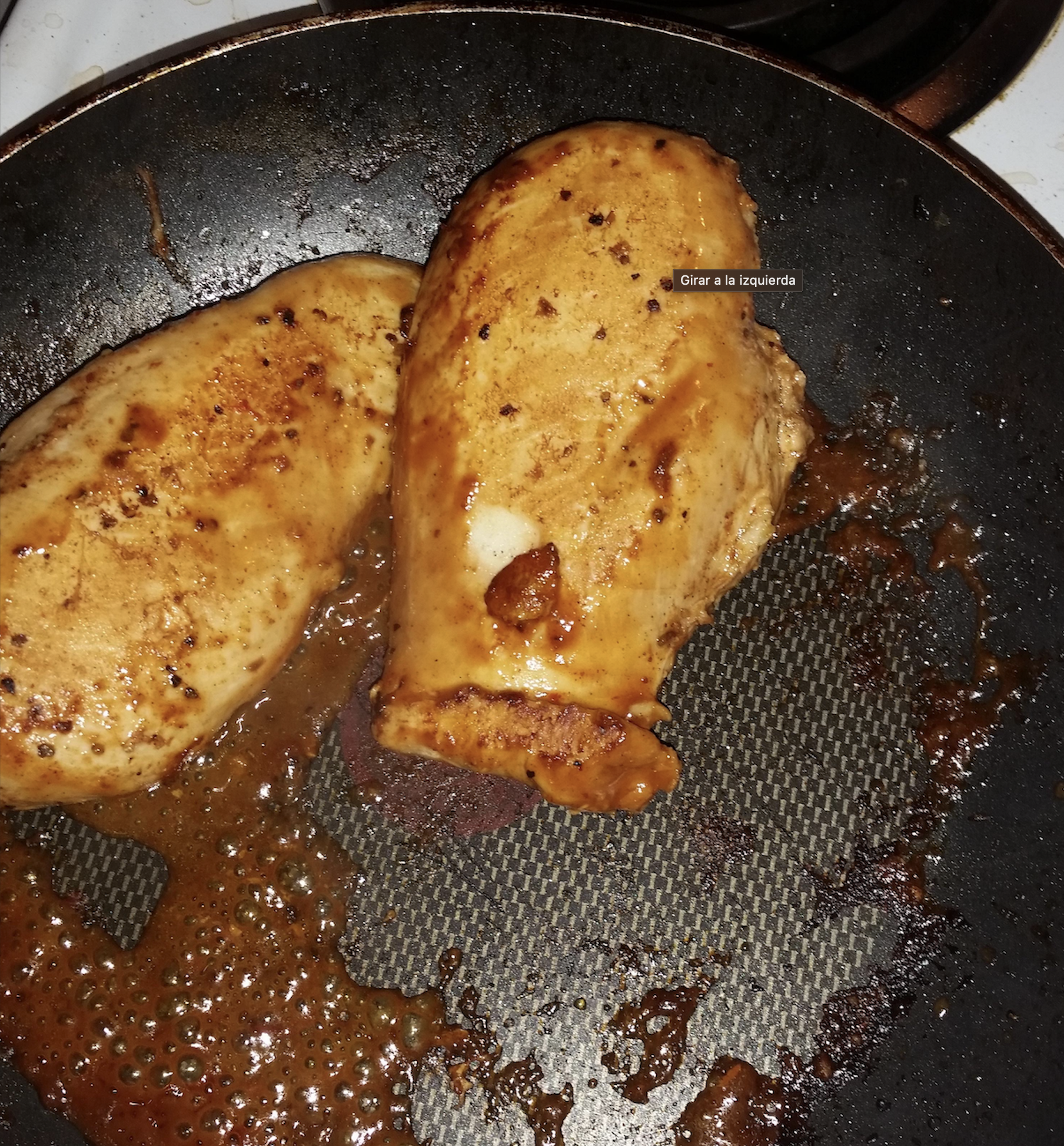 Two cooked chicken breasts with sauce in a black frying pan on a stovetop, with some bubbling sauce around the meat.