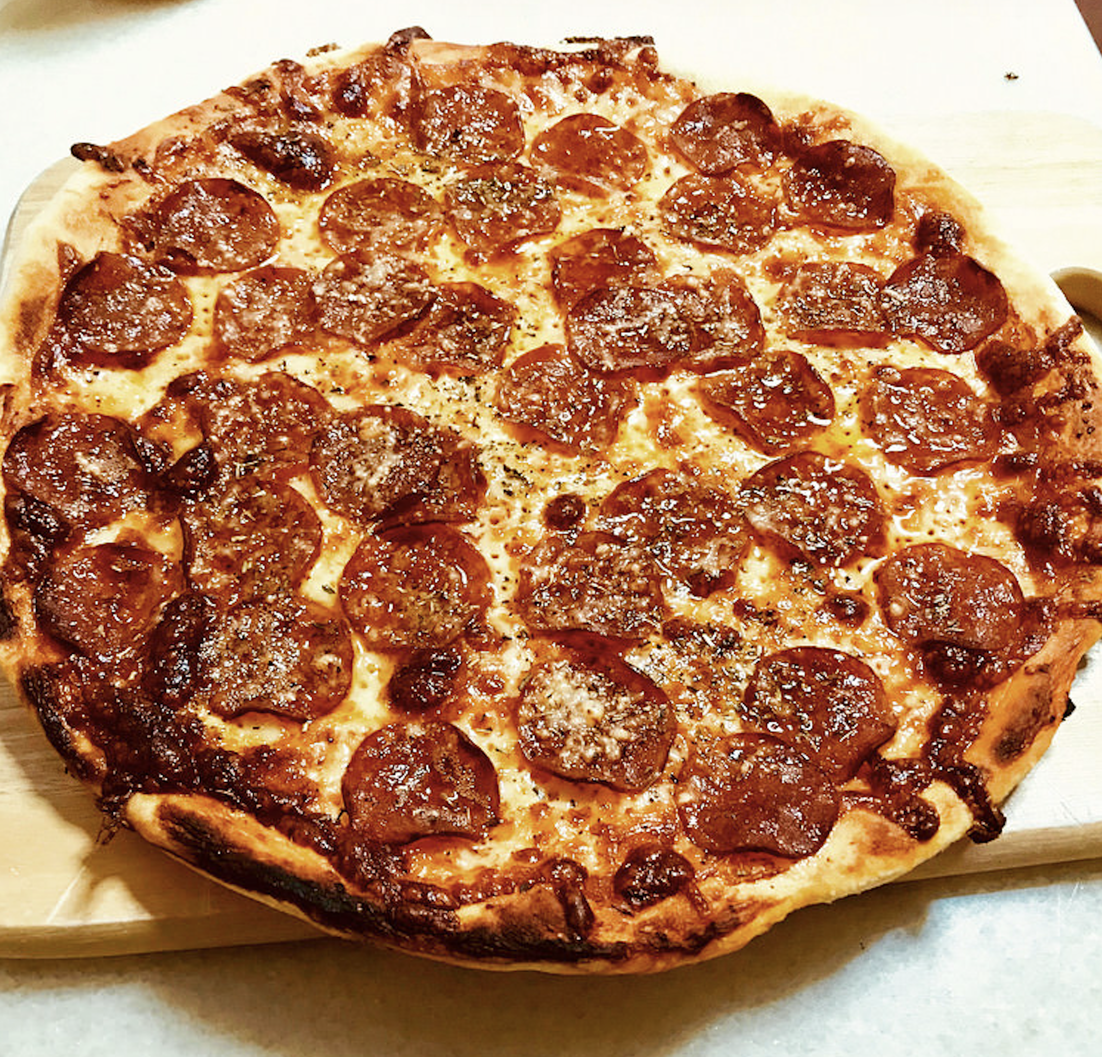 A freshly baked pepperoni pizza with a golden crust, melted cheese, and evenly spread pepperoni slices, sitting on a wooden board.