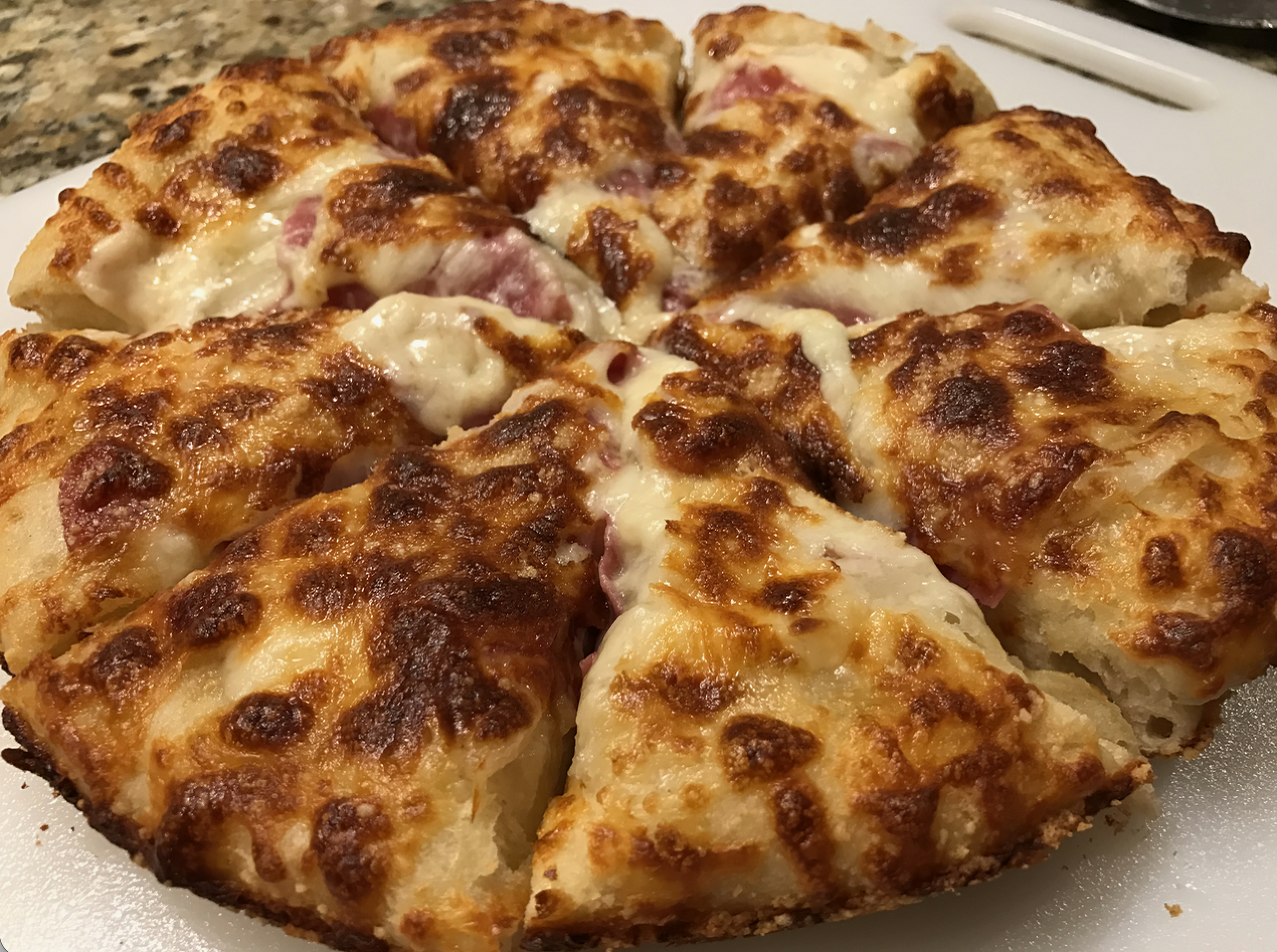 A close-up of a sliced cheese pizza with melted, golden-brown cheese and a thick, fluffy crust on a white cutting board.
