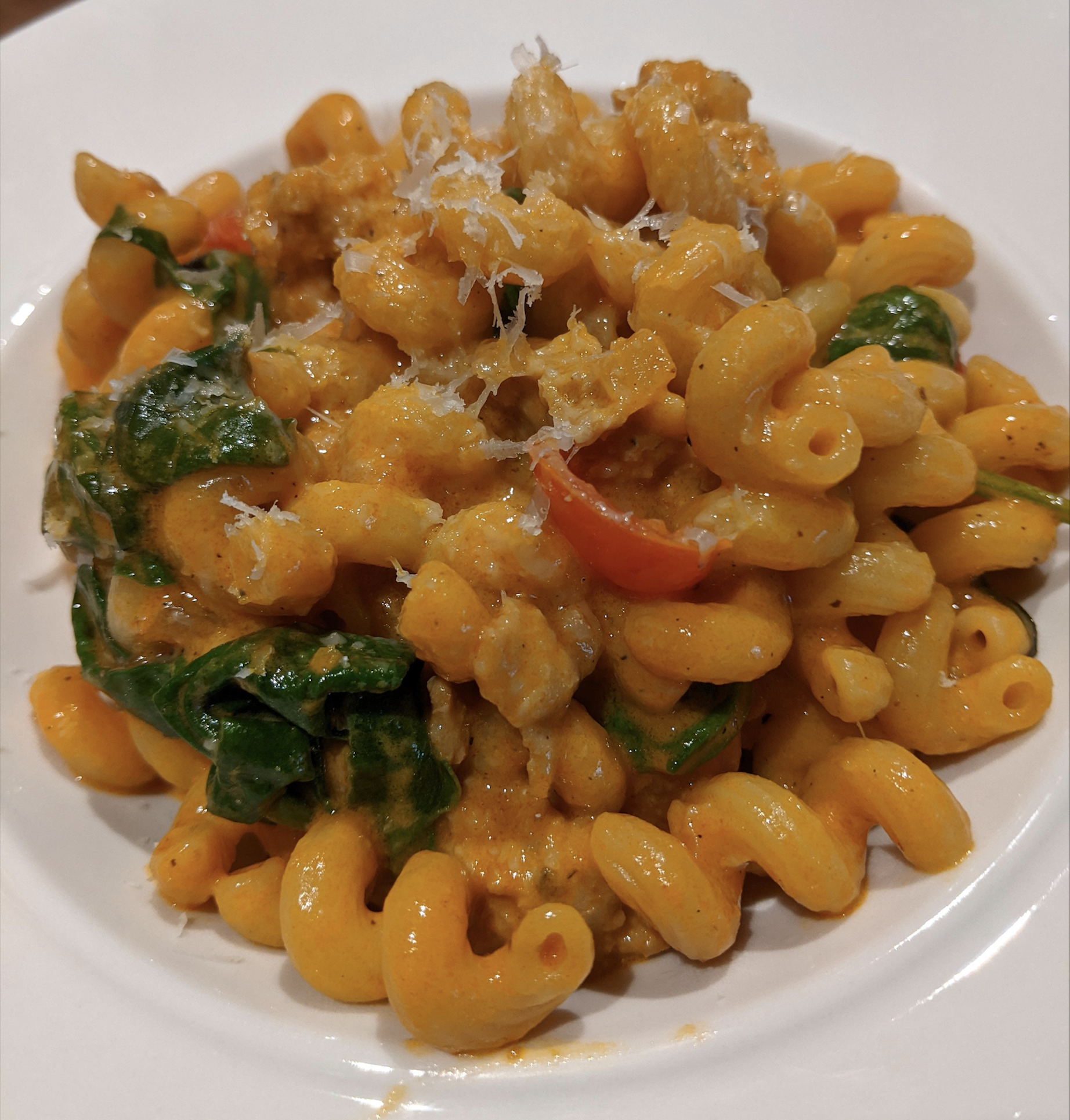A plate of creamy cavatappi pasta with pieces of chicken, spinach, red bell peppers, and grated cheese on top, served in a white bowl.