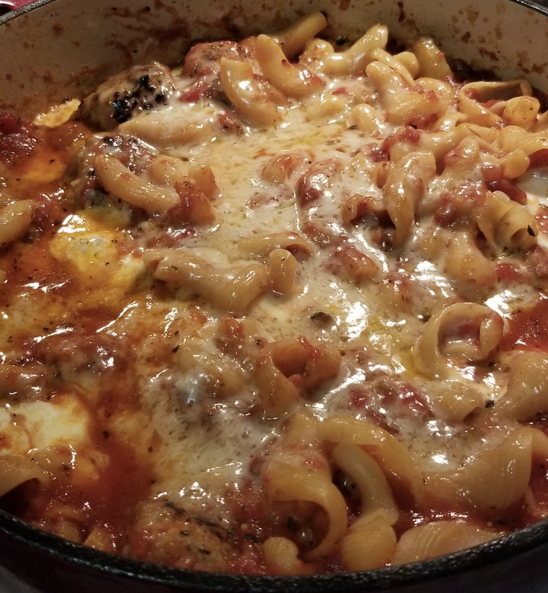 Baked pasta dish with corkscrew noodles, melted cheese, tomato sauce, and herbs in a round pan.