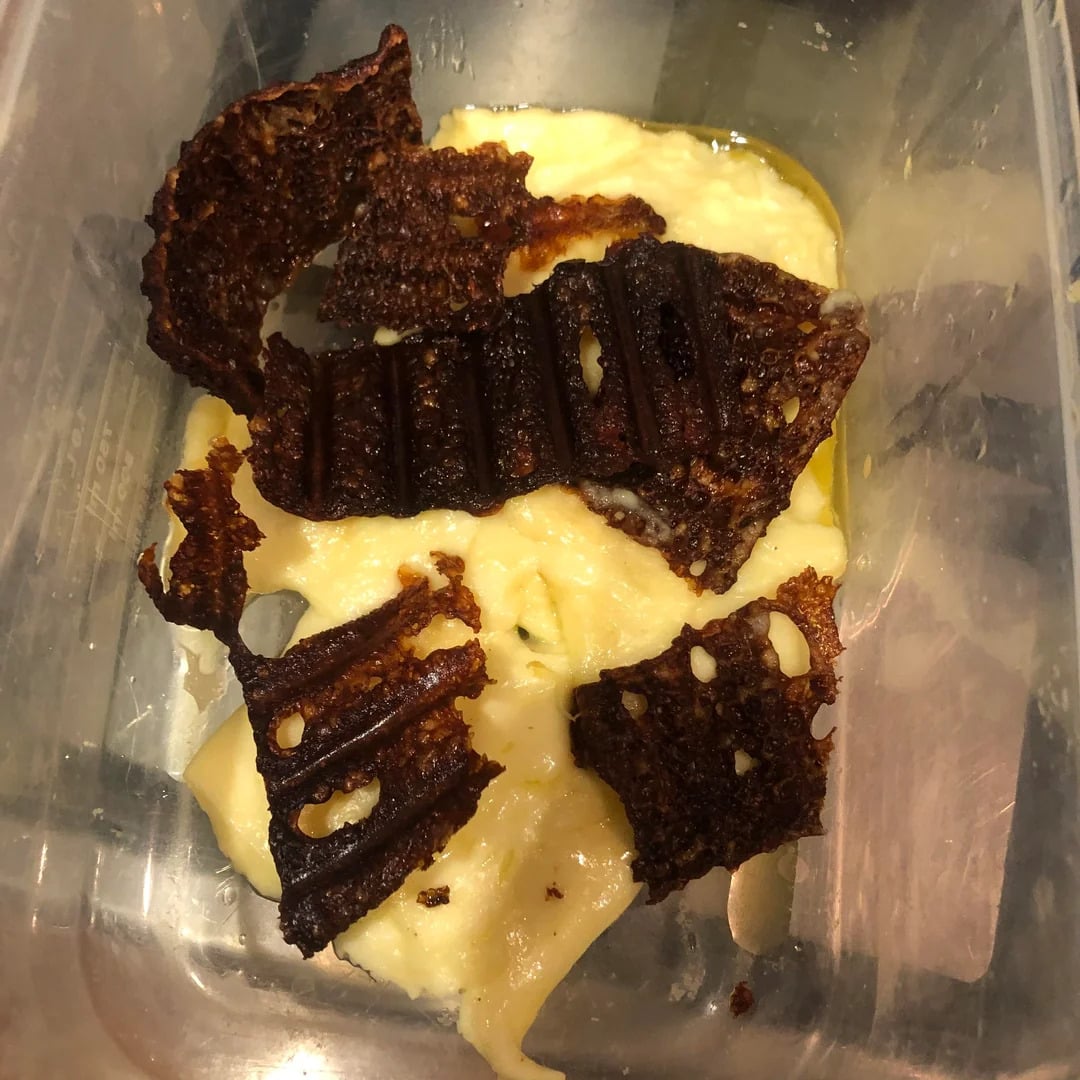 A plastic container holds creamy scrambled eggs topped with several pieces of burnt, crispy toast.