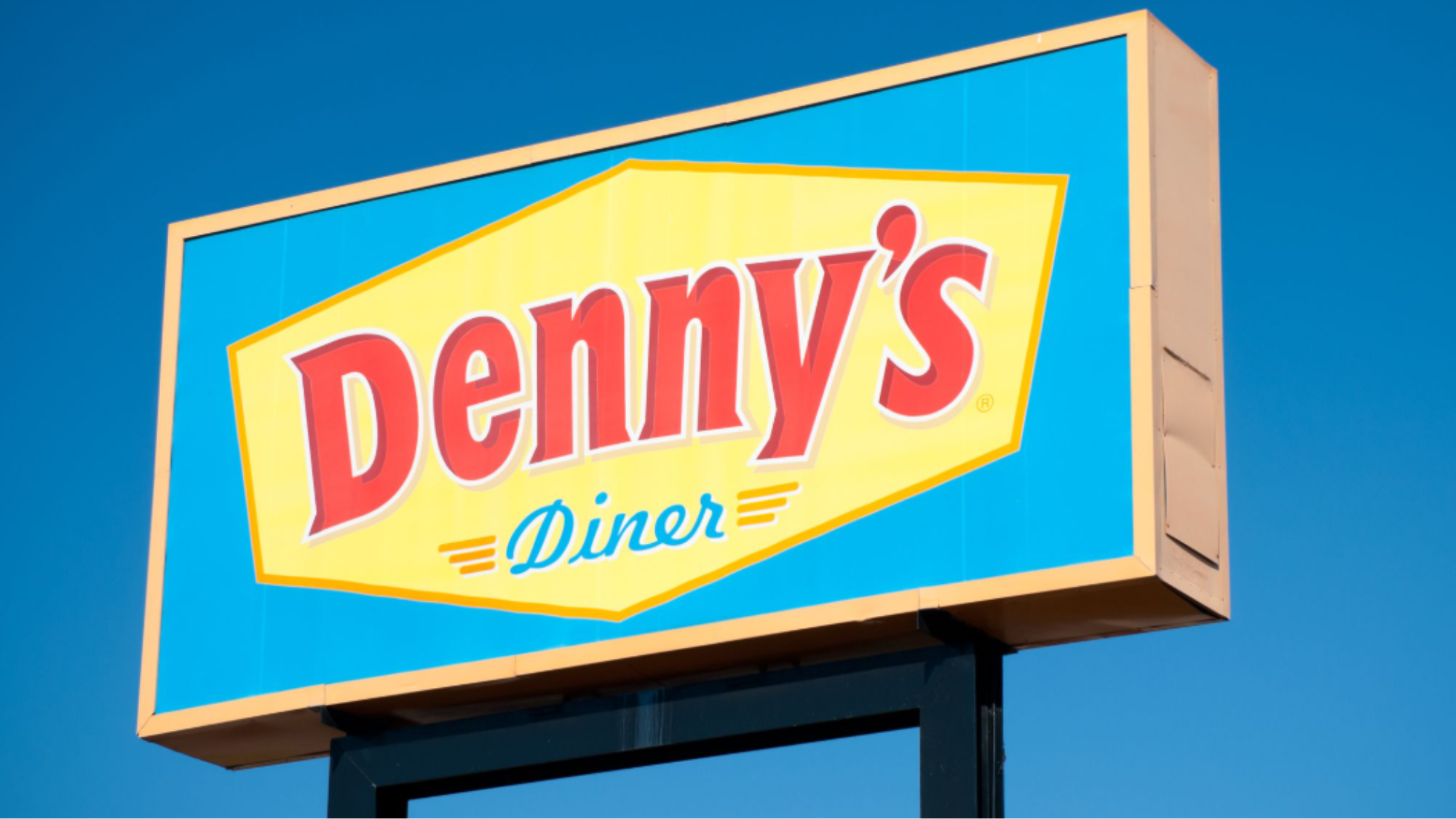 A brightly colored Denny's Diner sign with red and yellow lettering on a blue background, set against a clear blue sky—a nostalgic nod to fast-food chains from the '90s.