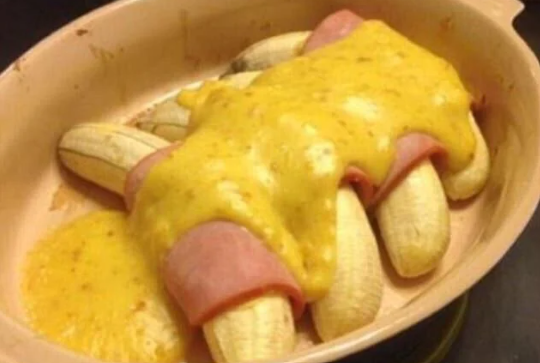 Several peeled bananas in a baking dish, each wrapped in a slice of ham and covered with melted yellow cheese sauce—a true example of epic cooking fails.