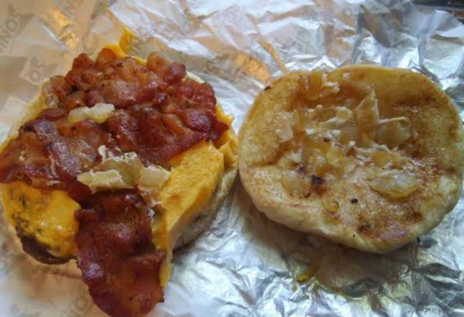A breakfast sandwich on a wrapper, with an open bun showing bacon, egg, and melted cheese on one side and grilled onions on the other half of the bun—bringing a morning twist to classic fast food burgers.