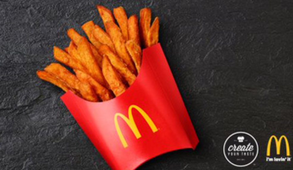 A red McDonald's fries container filled with seasoned fries sits on a dark surface, hinting at innovations from fast food test kitchens. Two McDonald's logos are visible in the bottom right corner.