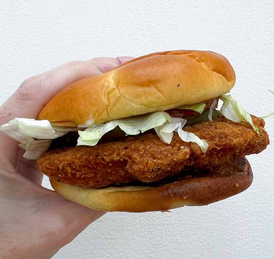 A hand holds a crispy chicken sandwich with lettuce and pickles between a soft, golden bun—one of the delicious Wendy's menu items—set against a plain white background.