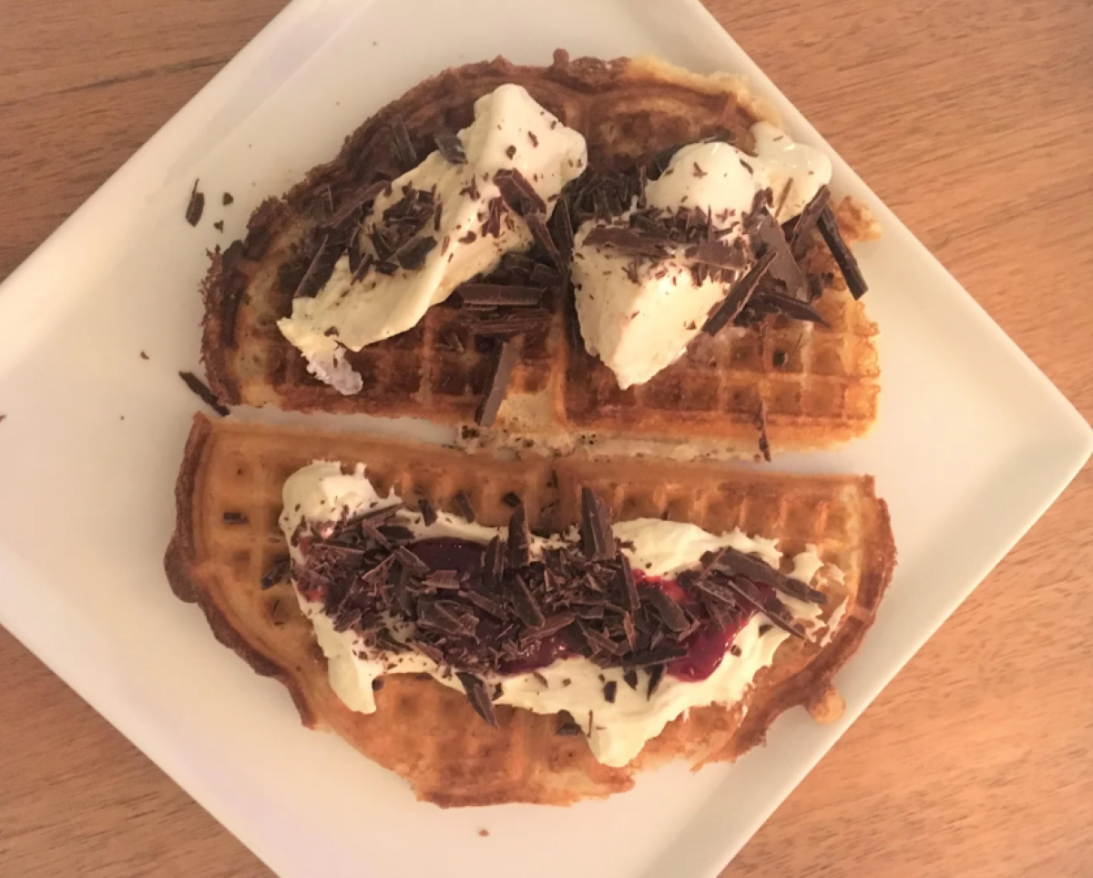 A plate with two pieces of waffle, each topped with whipped cream and chocolate shavings, on a light wooden table—perfect for anyone who loves homemade desserts.