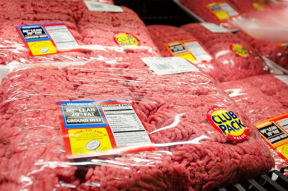 Packages of ground beef wrapped in plastic are displayed in a supermarket. The labels indicate “80% lean, 20% fat” and “Club Pack” value size. Nutrition facts and cooking instructions are visible on the packaging.