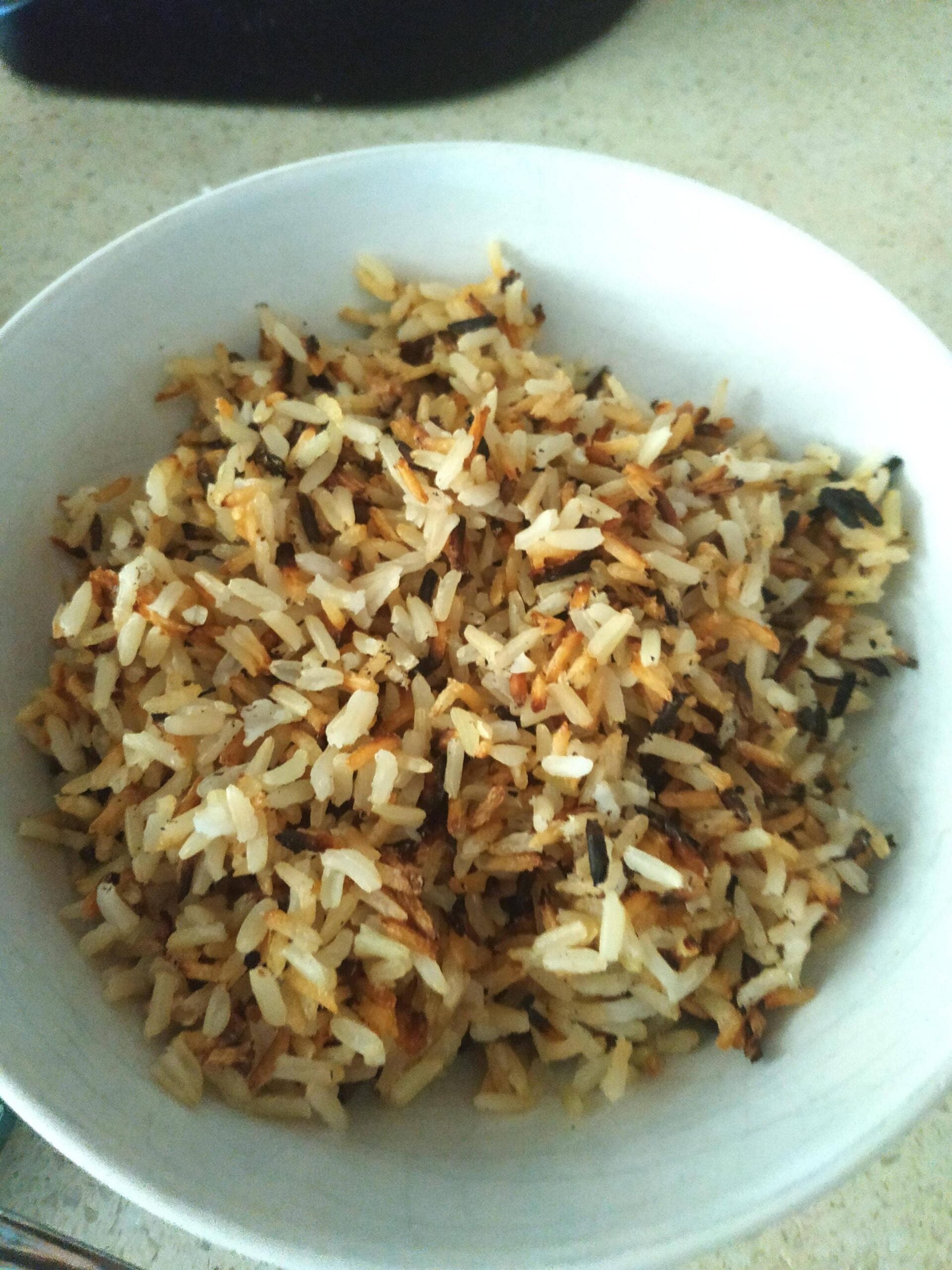 A white bowl filled with cooked rice, some grains visibly browned or slightly burnt, sitting on a countertop.