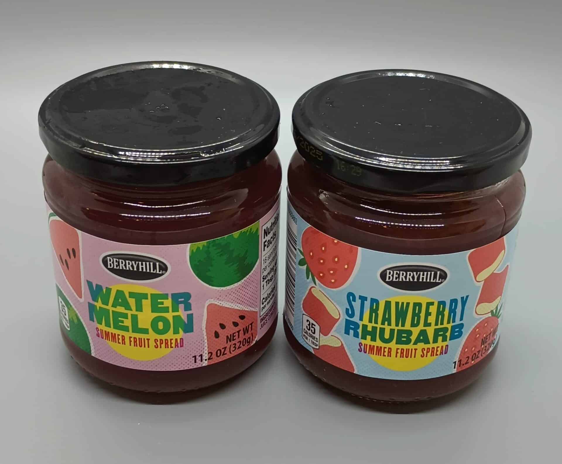 Two jars of Berryhill summer fruit spread: one labeled "Watermelon" and the other "Strawberry Rhubarb." Both jars are sealed with black lids and have colorful fruit-themed labels.