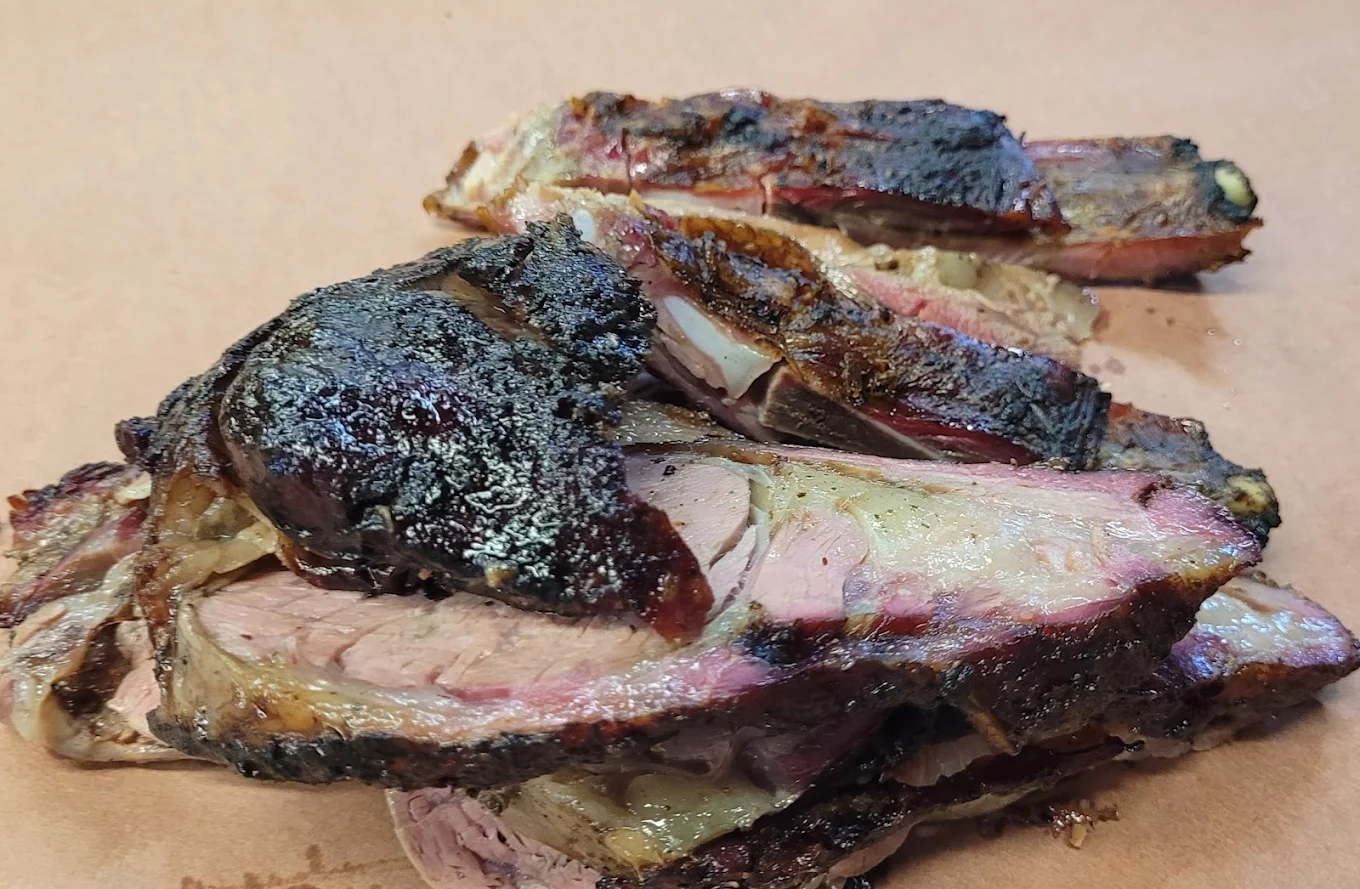Sliced, smoked beef brisket with a dark, charred bark and pink smoke ring, arranged on brown butcher paper.