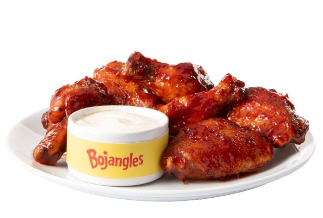 A plate of sauced chicken wings sits next to a Bojangles-branded cup filled with white dipping sauce, all on a white background, showcasing why Bojangles stands out among popular fried chicken chains.