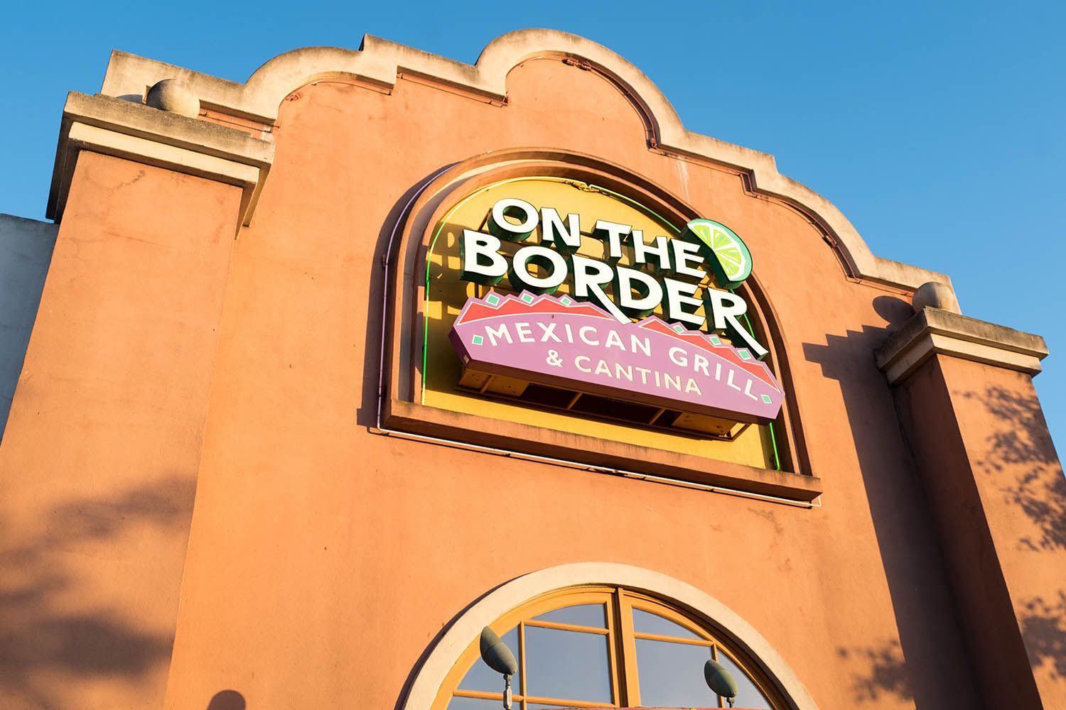 Exterior of an "On The Border Mexican Grill & Cantina" restaurant, with a large colorful sign on a stucco building under a blue sky.