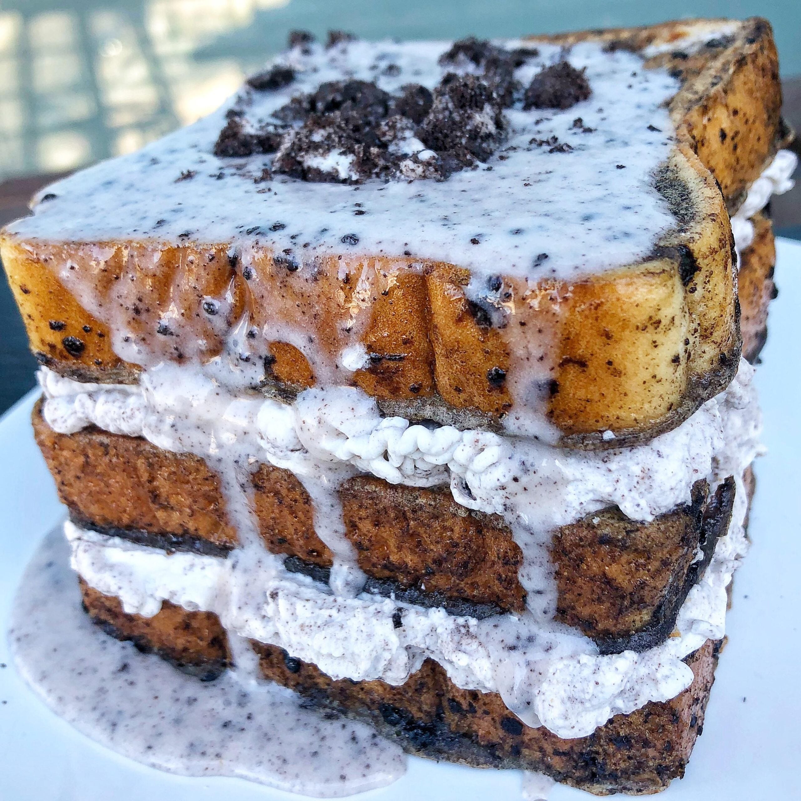 A thick, layered cookies-and-cream French toast topped with crumbled cookies and drizzled with creamy white sauce, served on a white plate.