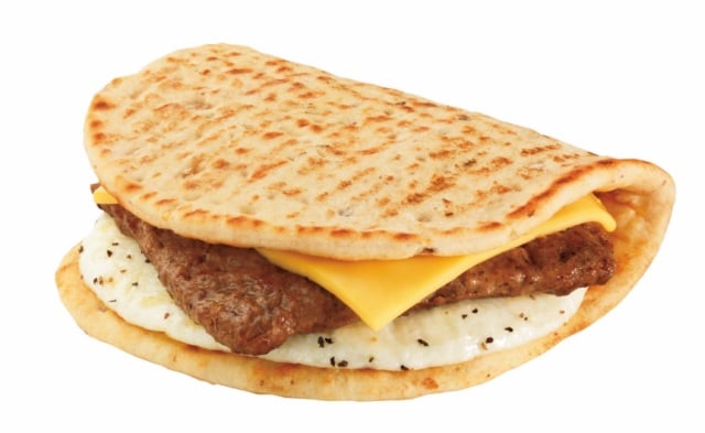 Flatbread sandwich with a folded egg patty, two slices of yellow cheese, and a sausage patty inside, all on a grilled flatbread against a white background.