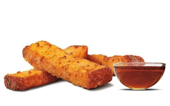 Three crispy hash brown sticks are stacked next to a clear glass bowl filled with a golden brown dipping sauce, set against a white background.