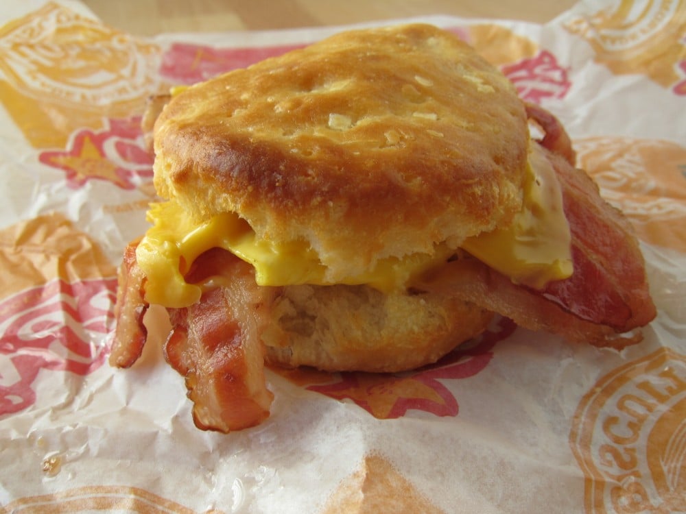 A biscuit sandwich filled with crispy bacon and melted cheese sits on a fast food wrapper.