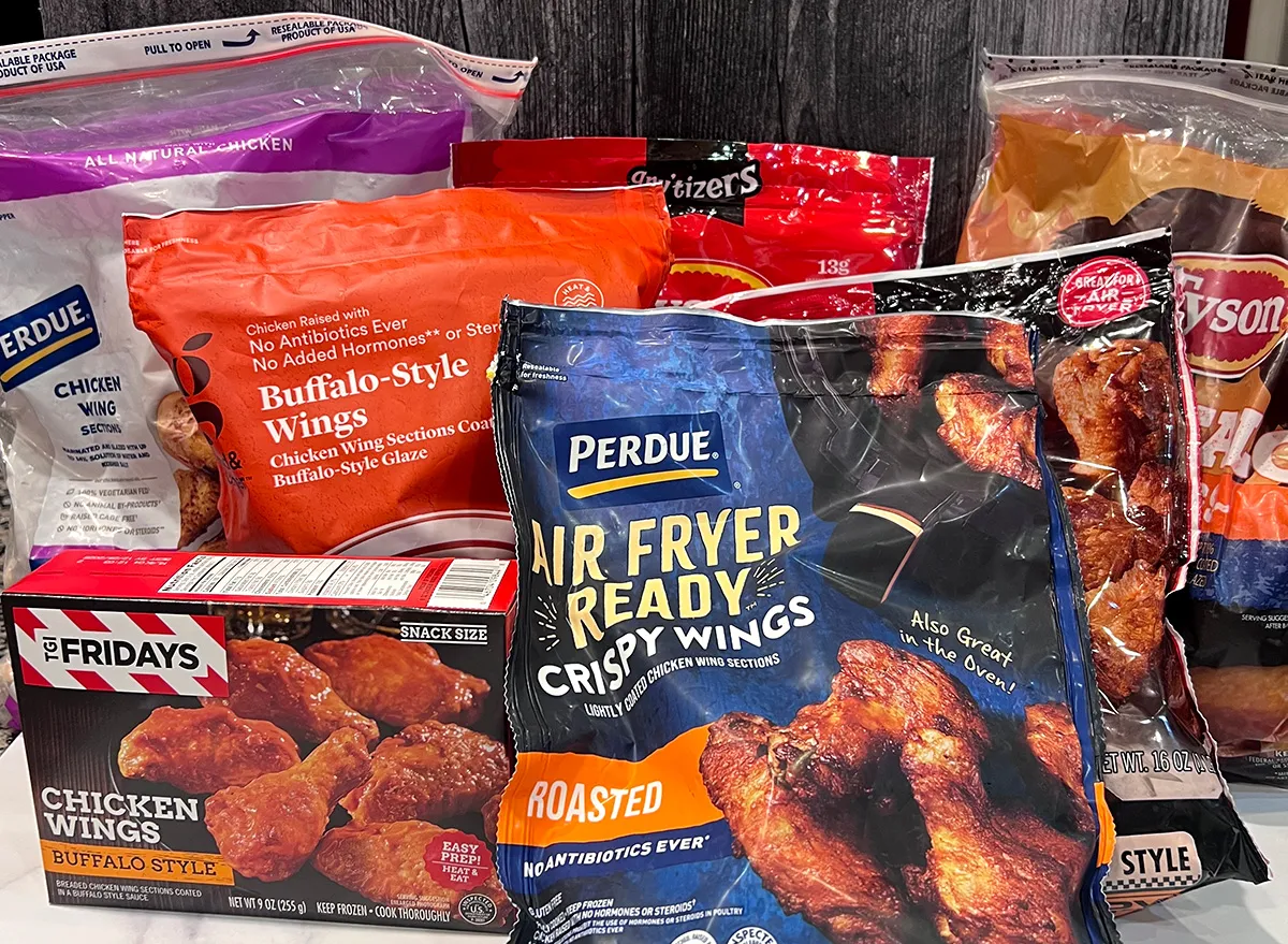Assorted frozen chicken wing packages, including Perdue, TGI Fridays, and Tyson brands, are stacked together on a kitchen countertop. The bags display various flavors like buffalo-style and roasted.