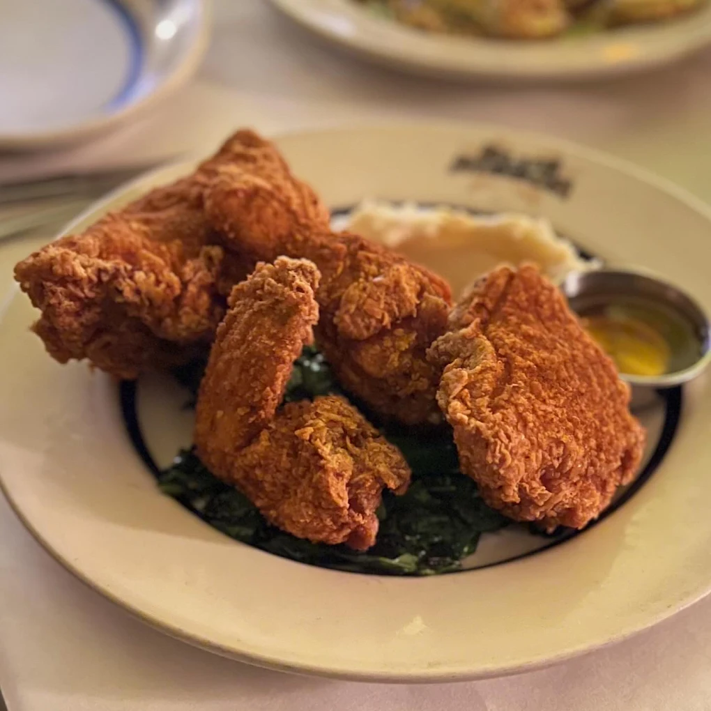 Three pieces of crispy fried chicken served on a bed of greens with a side of mashed potatoes and gravy, presented on a white plate.