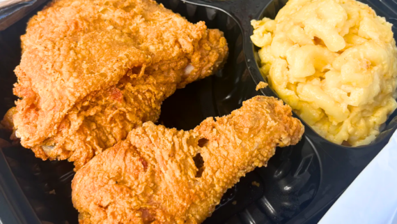 Two pieces of crispy fried chicken, a classic favorite among fried chicken dishes, paired with a serving of creamy macaroni and cheese in a black plastic tray.
