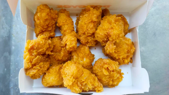 A box filled with several pieces of crispy, golden-brown fried chicken and fast-food chicken nuggets on a gray surface.